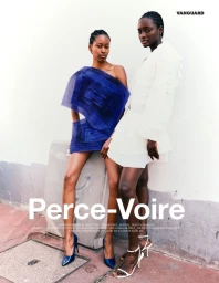 Two female models posing outdoors against a pale wall for Vanguard Magazine, wearing structural blue and white outfits.