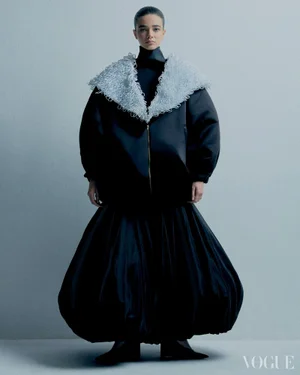 Model wearing a black puffed skirt and jacket with a textured white collar against a grey studio backdrop for Vogue Brasil.