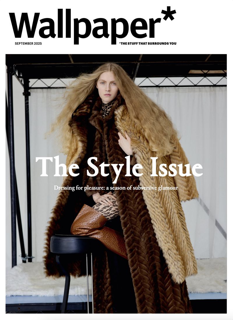 Female model with long blonde hair wearing a fur coat, seated on a stool, on a magazine cover.