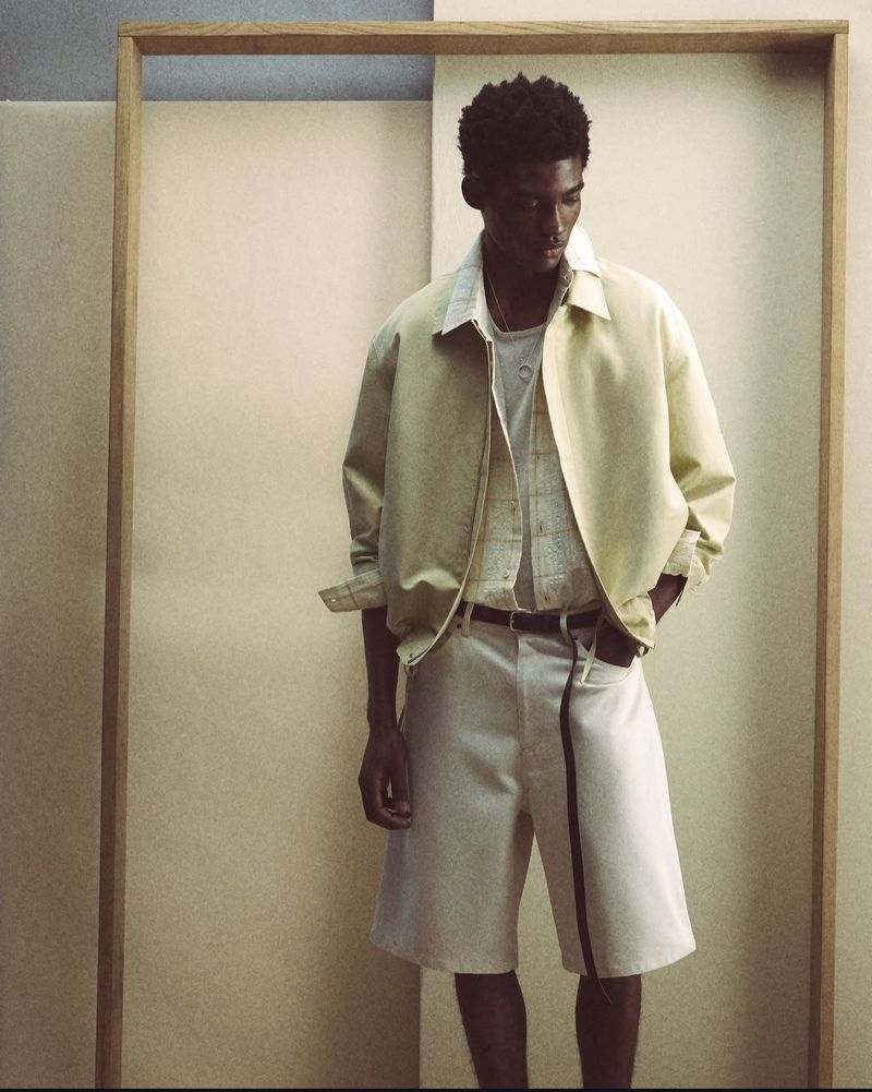 Fashion shot of a stylish man wearing a yellow jacket and white shorts in a minimalist setting with a geometric frame.