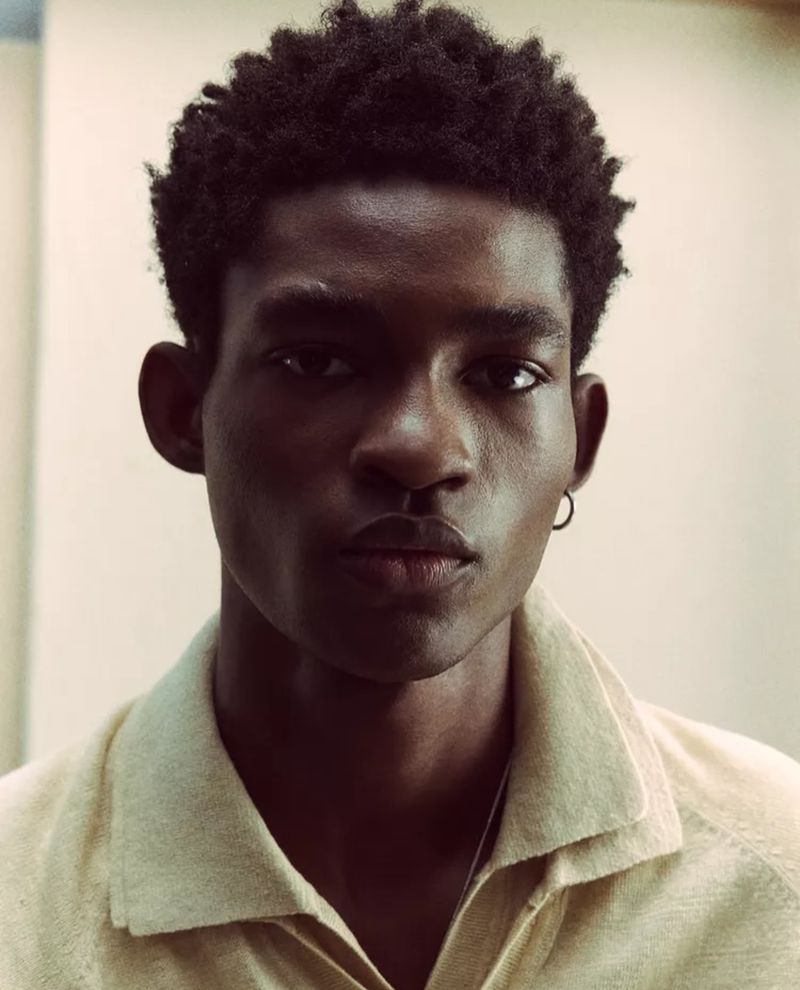 Portrait of a Black man with natural hair, wearing a collared shirt, with a neutral expression against a plain background in a studio setting.
