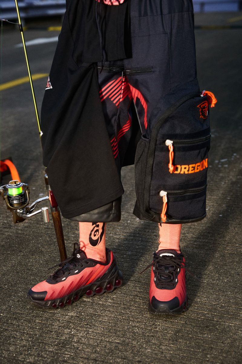 Person wearing black and red sneakers and black cargo shorts stands on grey pavement. Fishing pole in the background.