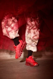 Red sneakers worn with patterned trousers and layered red tulle fabric in a commercial footwear campaign.