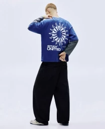 Model seen from behind wearing a blue graphic t-shirt and black trousers against a plain white background.