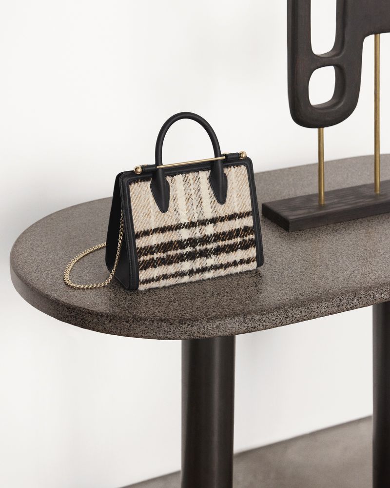 Striped fabric handbag with black trim and gold chain strap on a mottled grey table next to a dark brown abstract sculpture.
