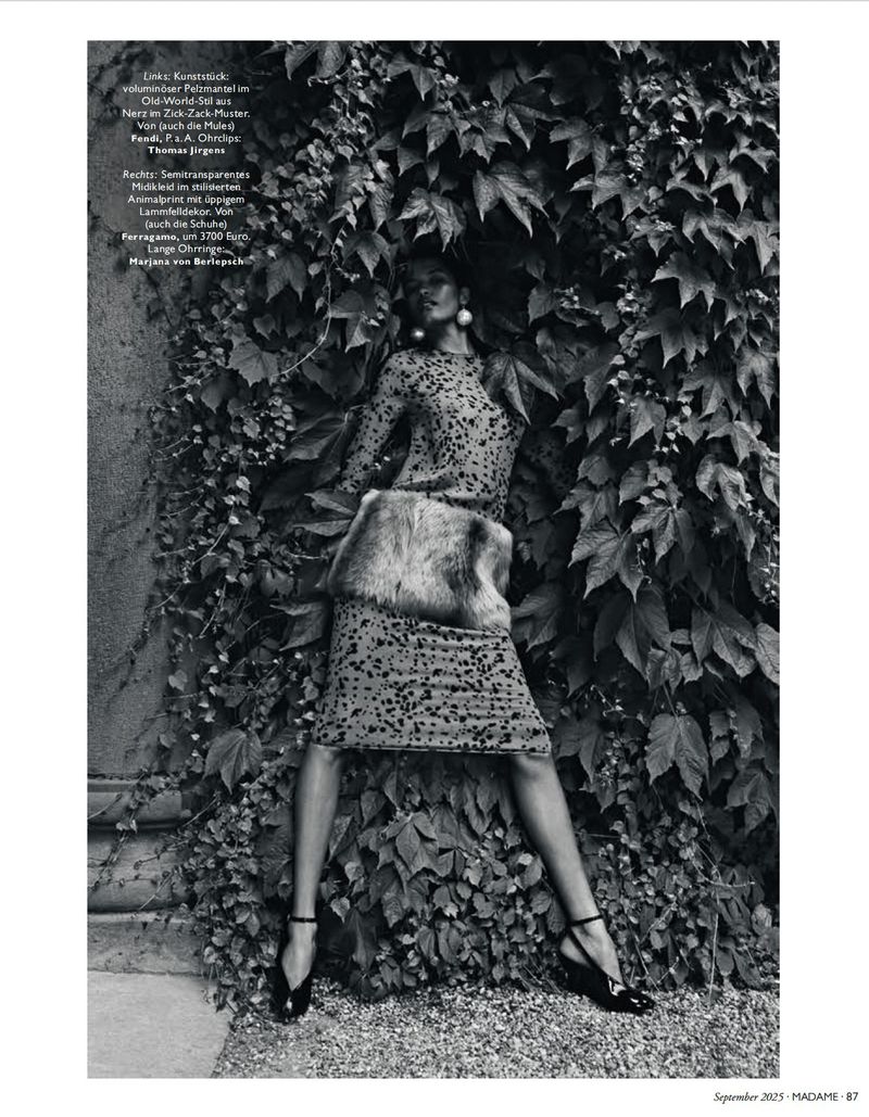 Monochrome fashion shot of a woman in a patterned dress with fur detail posing amidst ivy, showcasing editorial style and outdoor setting.