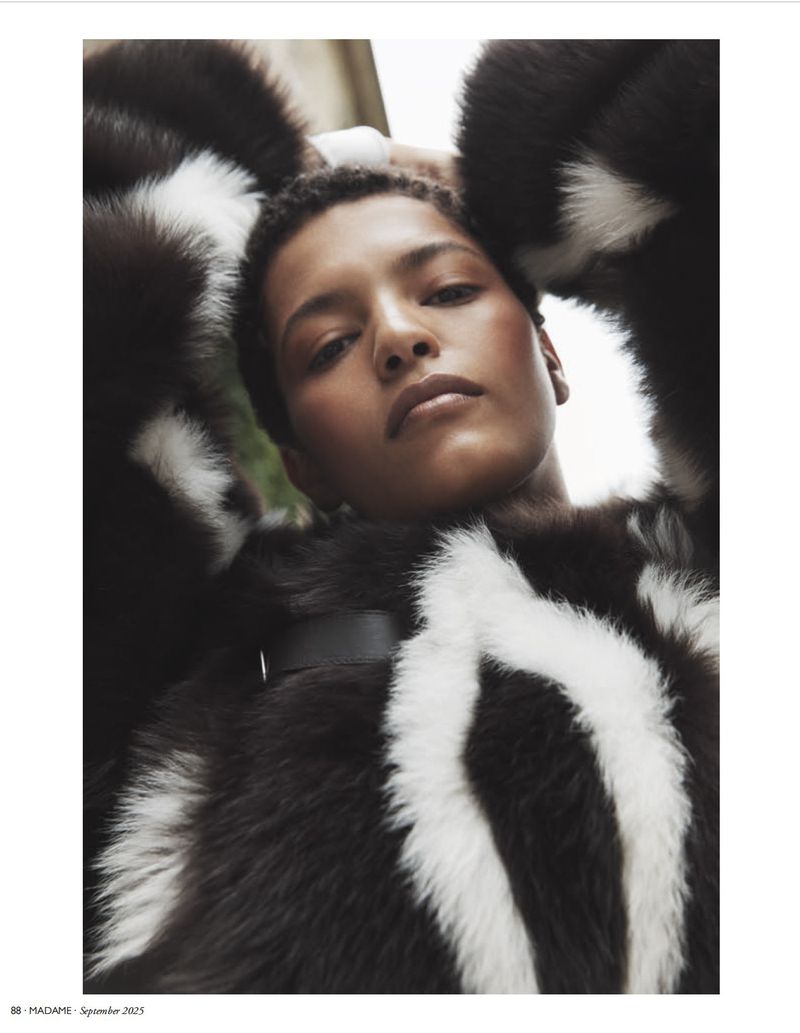 Fashion editorial headshot of a woman in a black-and-white fur coat, eyes toward the camera, in a soft outdoor light.