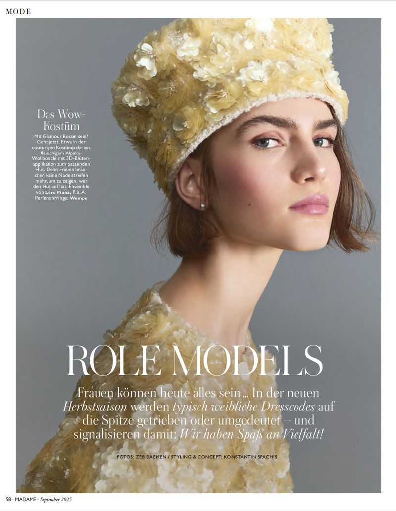 Close-up shot of a fair-skinned young woman wearing a floral-embellished hat and dress in a fashion editorial style, softly lit.