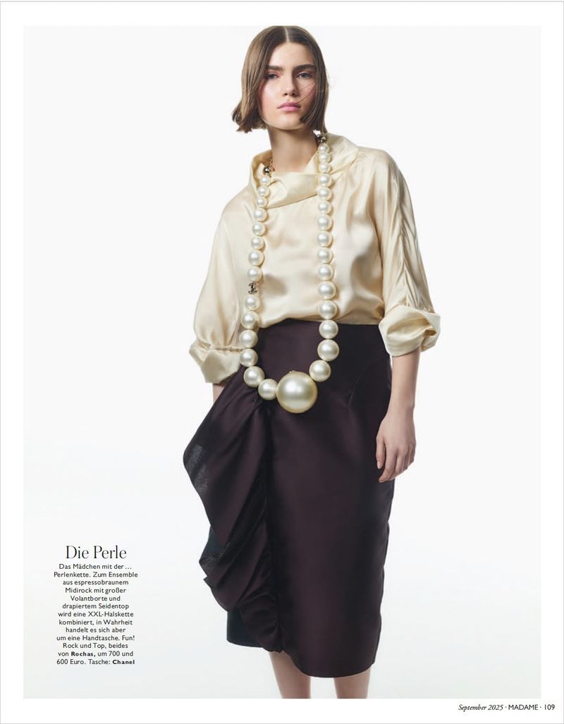 Fashion editorial shot of a stylish woman wearing a cream-colored blouse, a brown skirt with ruffles, and an oversized pearl necklace.