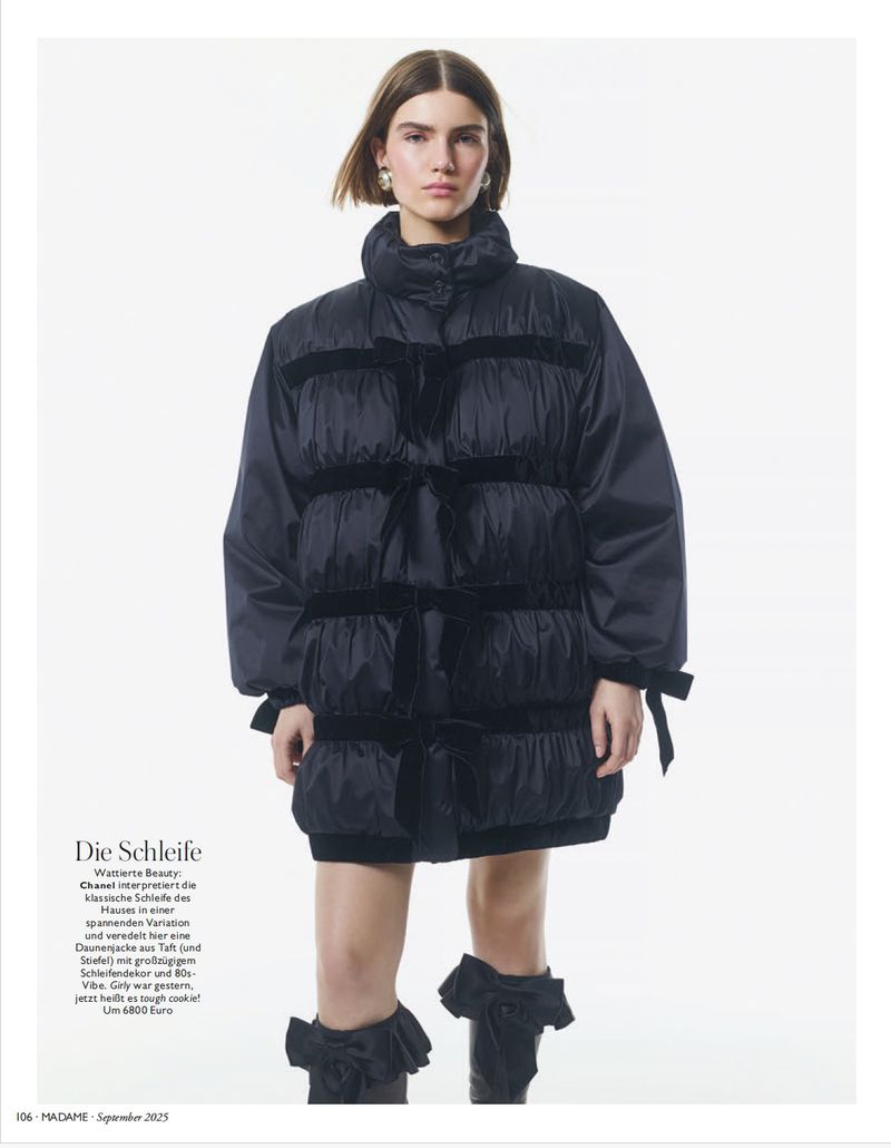 Fashion editorial shot of a woman wearing a black puffer jacket dress and knee-high boots with ruffles against a white background.