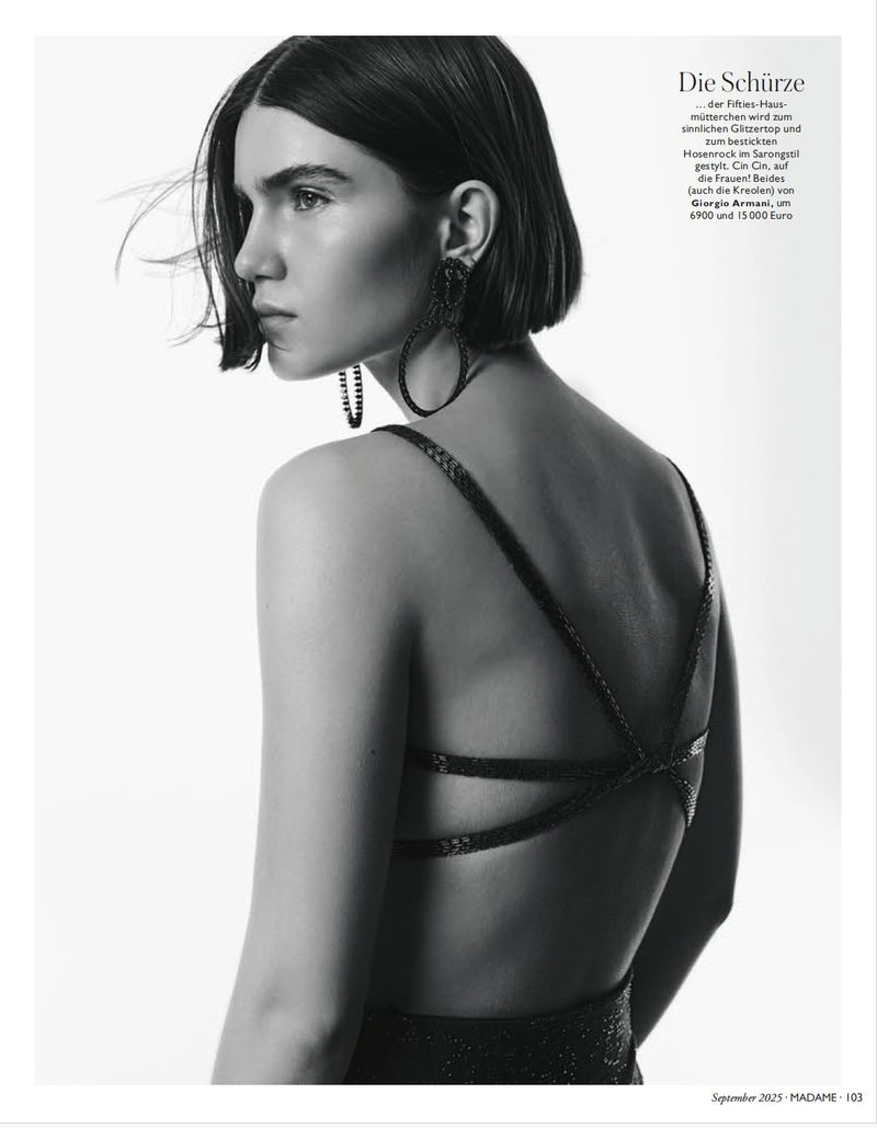 Monochrome fashion portrait of a slender woman with short dark hair wearing an elegant dress and large hoop earrings in a studio.
