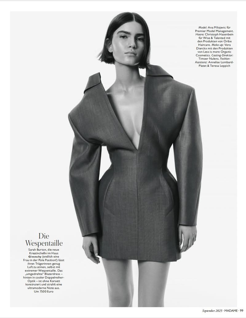 A striking portrait of a model wearing an avant-garde grey jacket dress with exaggerated shoulders in a studio fashion shot.