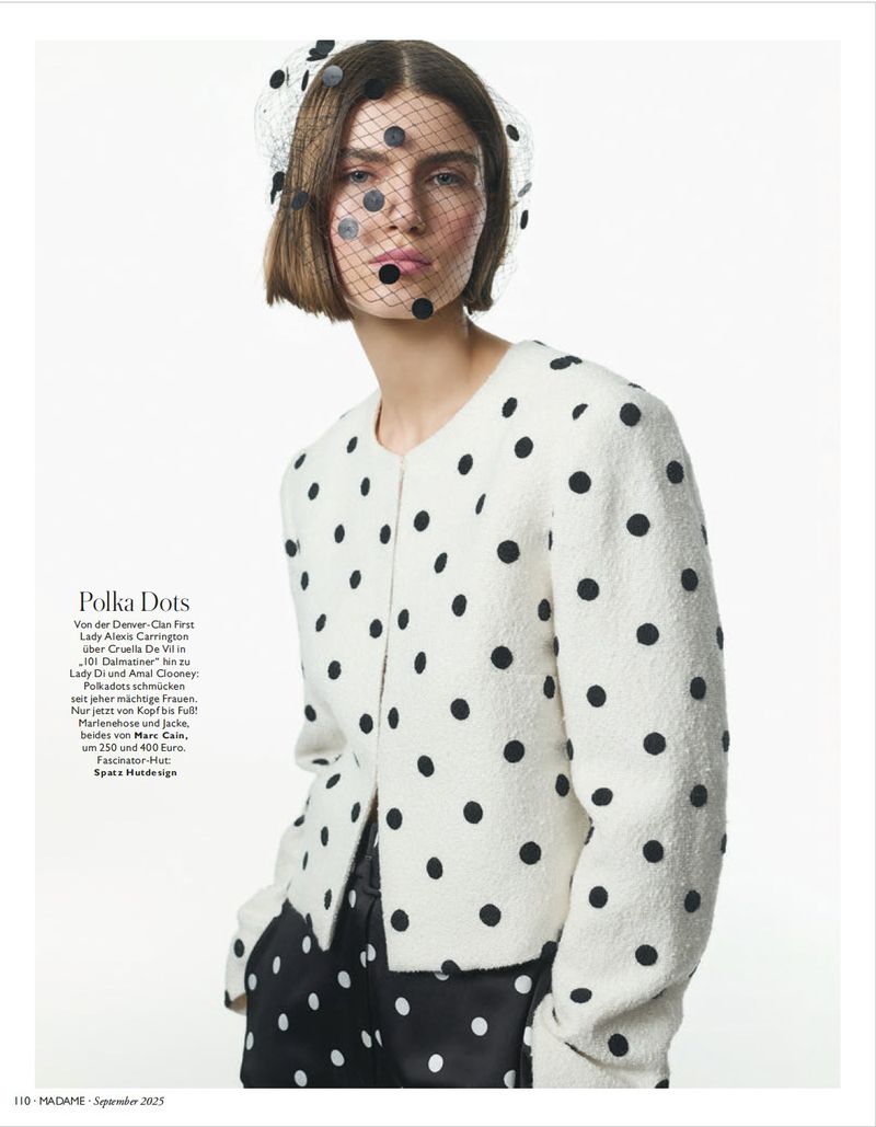 Fashion editorial shot of a woman wearing a white polka dot jacket and a black polka dot veil against a white backdrop.