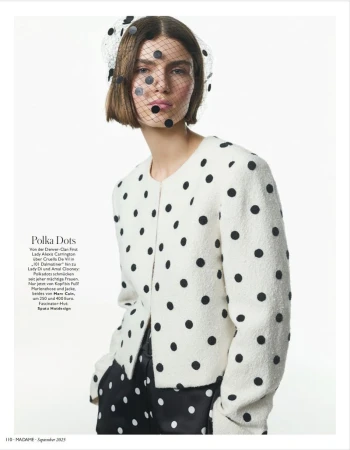 Fashion editorial shot of a woman wearing a white polka dot jacket and a black polka dot veil against a white backdrop.