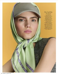 Close-up portrait of a female model wearing a light green silk headscarf tied under the chin with a grey baseball cap on top.