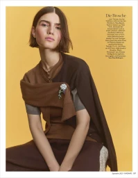 Model in brown layered knitwear with a decorative brooch against a warm yellow background for Madame Germany editorial.
