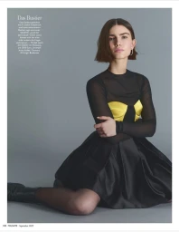Model with short dark hair wearing a black dress with a yellow bustier against a grey background for Madame Germany Role Models.