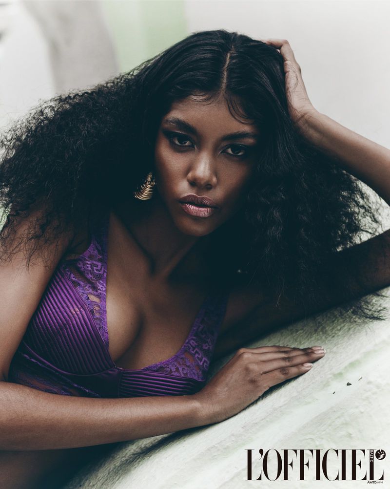 Portrait of a woman with dark hair and purple lingerie, laying on a green surface, wearing gold earrings, shot with a close-up framing.