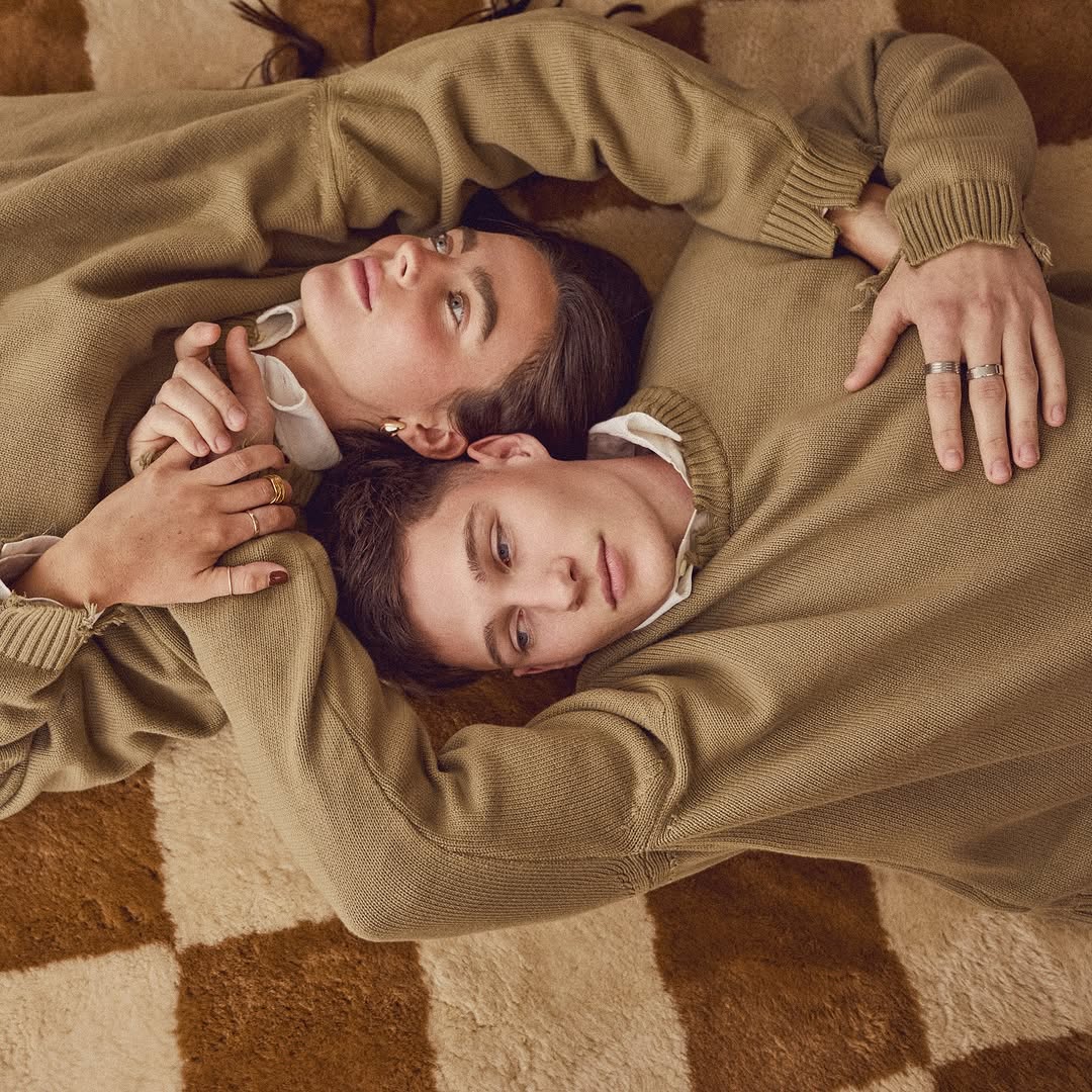 A young couple in matching sweaters poses lying on a checkered rug, creating a soft and cozy atmosphere in this portrait.