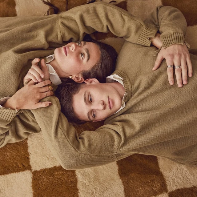A young couple in matching sweaters poses lying on a checkered rug, creating a soft and cozy atmosphere in this portrait.