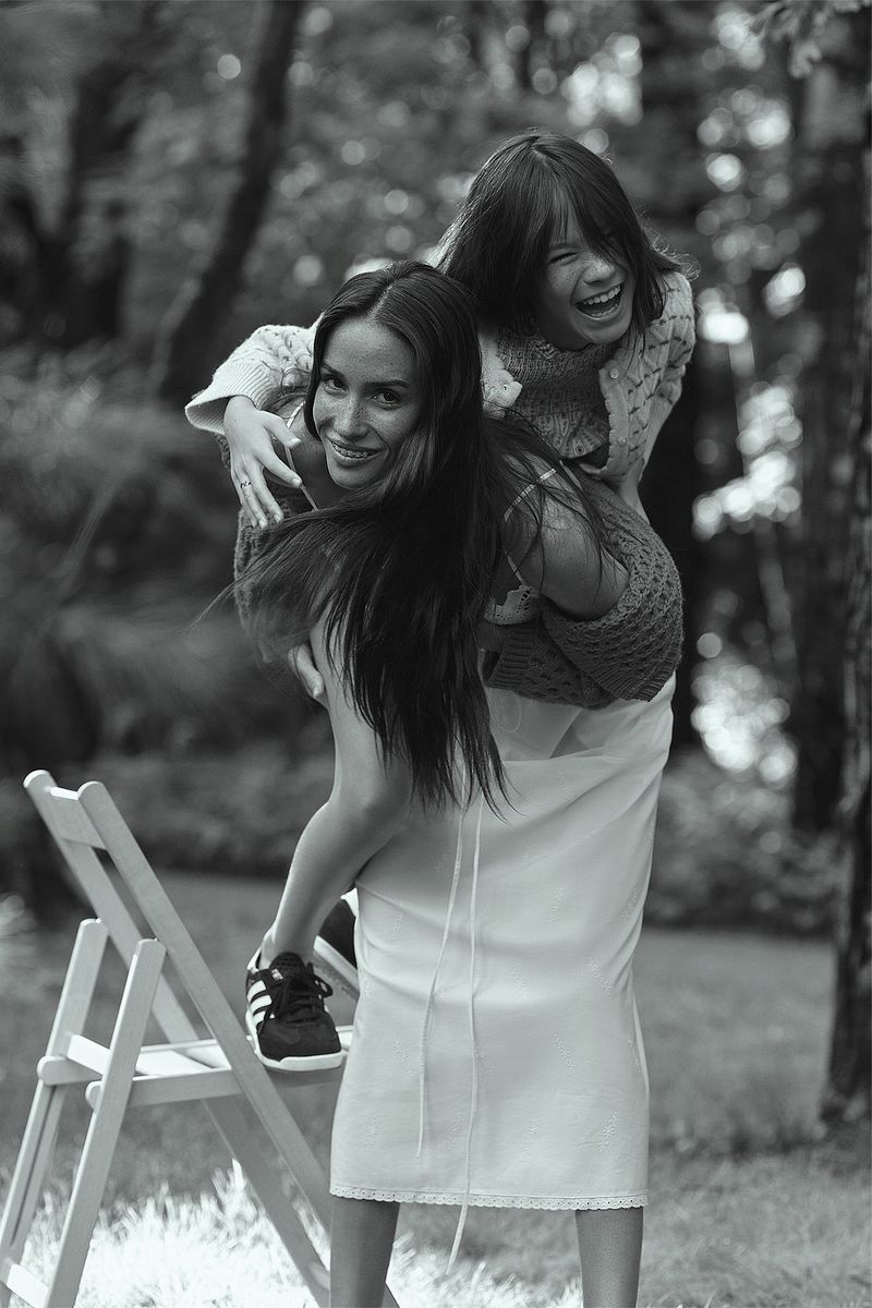 Black and white portrait of a smiling woman carrying a laughing child piggyback style in a green outdoor setting with trees.