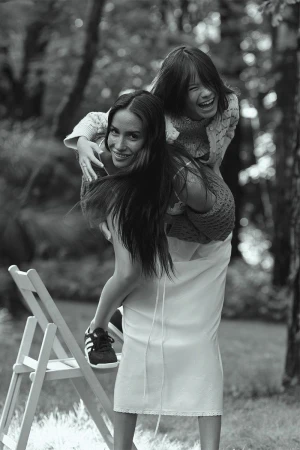 Black and white portrait of a smiling woman carrying a laughing child piggyback style in a green outdoor setting with trees.