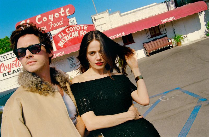 Outdoor shot of a stylish couple posing in front of El Coyote restaurant in Los Angeles, CA, under a clear blue sky on a sunny day.