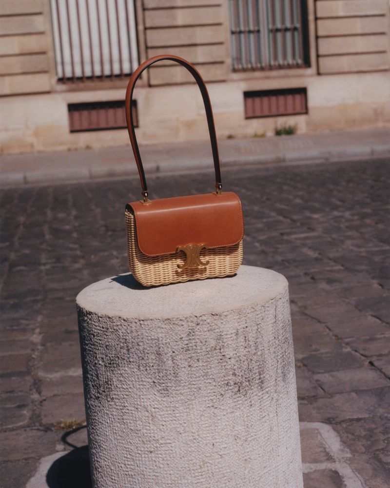 Fashionable Celine handbag featuring brown leather and woven straw textures placed on a weathered stone column in an outdoor urban setting.