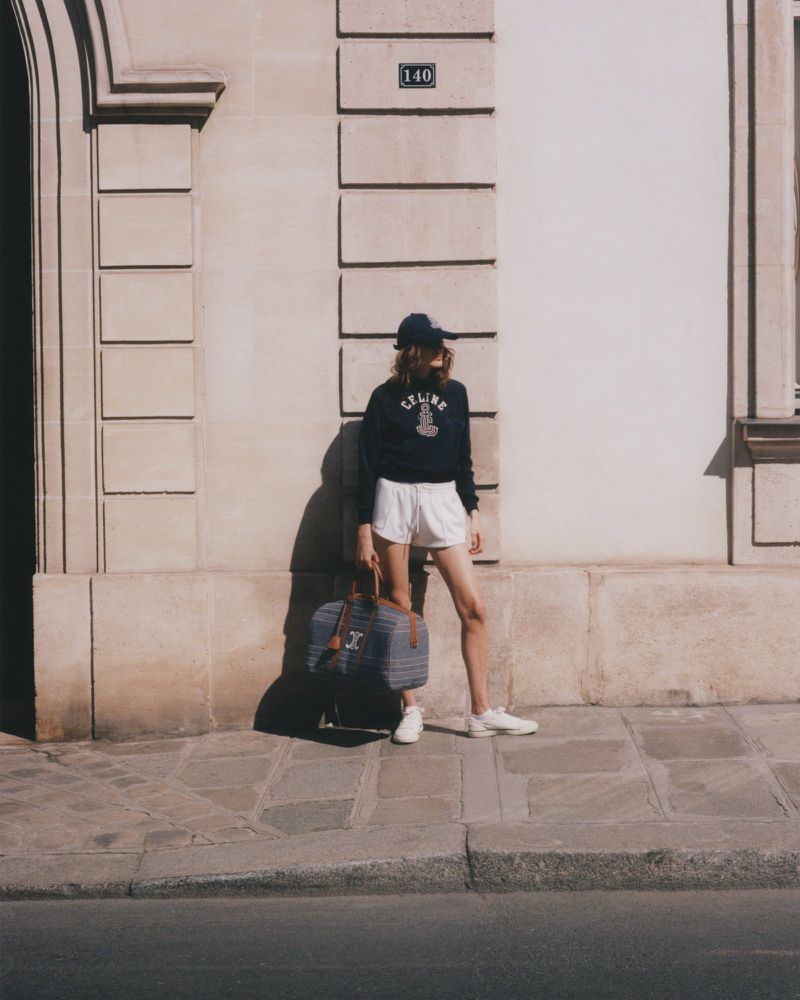 Woman in casual athleisure outfit with duffel bag poses against stone facade in natural light, capturing a blend of fashion and lifestyle.