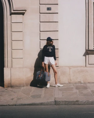 Woman in casual athleisure outfit with duffel bag poses against stone facade in natural light, capturing a blend of fashion and lifestyle.