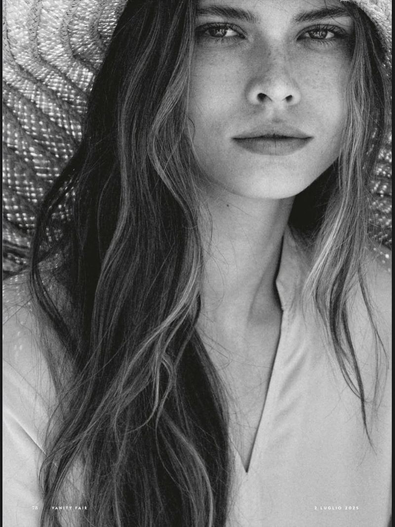 Striking black-and-white portrait of a woman wearing a straw hat, her wavy hair cascading down, captured in a close-up studio shot.