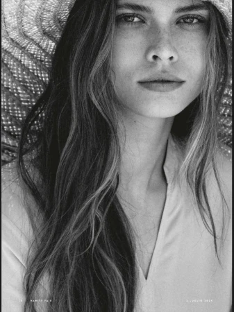 Striking black-and-white portrait of a woman wearing a straw hat, her wavy hair cascading down, captured in a close-up studio shot.