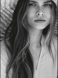 Close-up black and white portrait of model Zoe Petit wearing a wide-brim woven straw hat and v-neck top for Vanity Fair Italia.