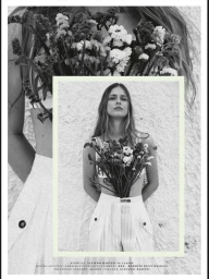 Black and white editorial portrait of a female model holding a large bouquet of wildflowers against a textured wall.
