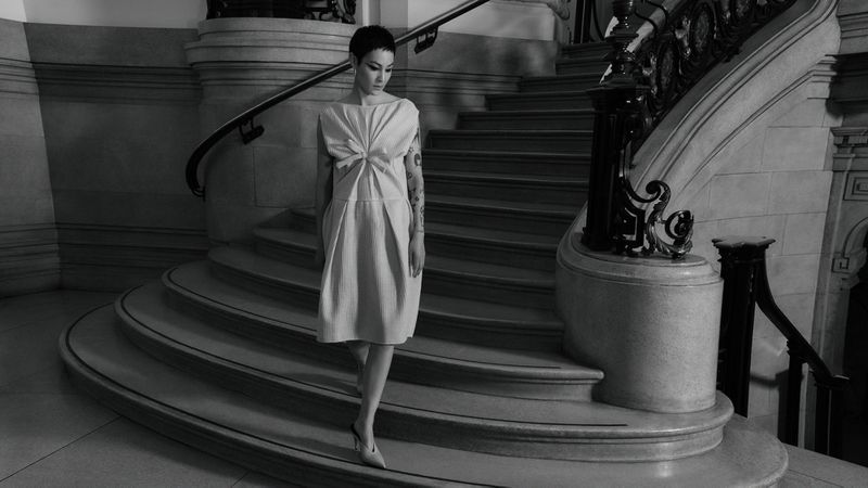 Elegant woman in a dress descends a marble staircase with wrought iron railing, captured in monochrome tones.