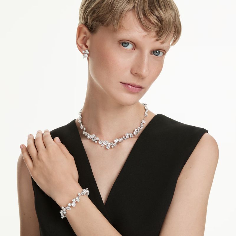 Adult female poses indoors wearing a black top and jewelry set including earrings, necklace, and bracelet against a white background.