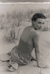 Model Hazel Jane seated on coastal sand dunes wearing a smocked strappy summer dress looking over her shoulder.