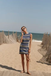Model in a blue striped sleeveless dress and sunglasses standing on a sandy beach path