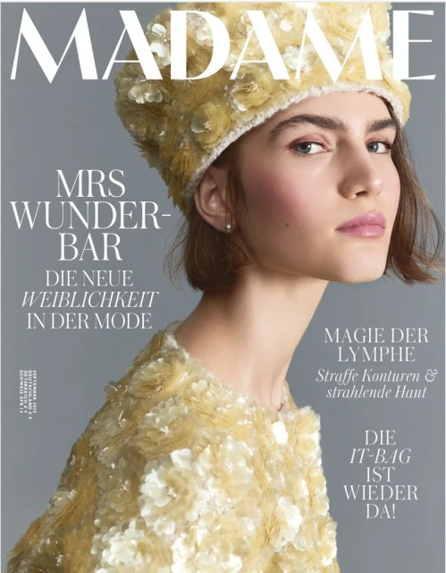 Magazine cover featuring a woman with fair skin and light brown hair wearing a yellow floral hat and matching sequined jacket.