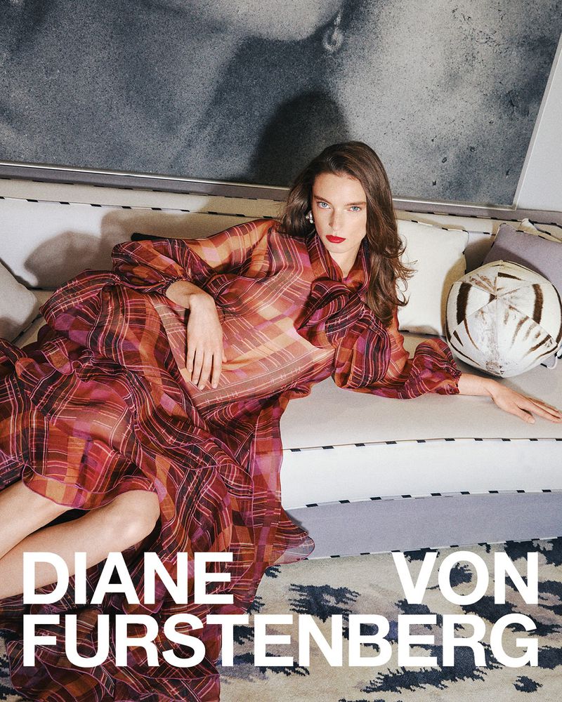 A woman lies on a sofa wearing a plaid dress in a fashion editorial for Diane von Furstenberg in an indoor setting.