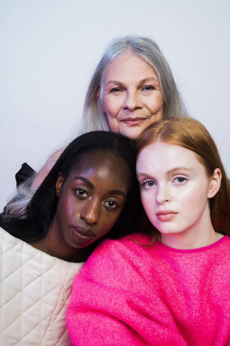Close-up studio portrait featuring three diverse women with varying skin tones and hair colors, posing together against a soft white backdrop.