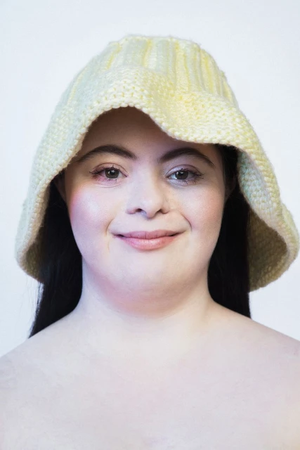 Close-up portrait of a smiling woman wearing a yellow knit hat against a white background, showcasing beauty and headwear.
