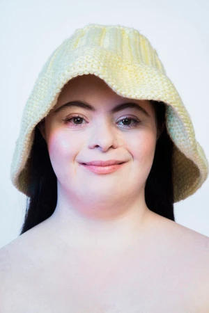 Close-up portrait of model Ellie Goldstein wearing a pale yellow crocheted bucket hat against a white background