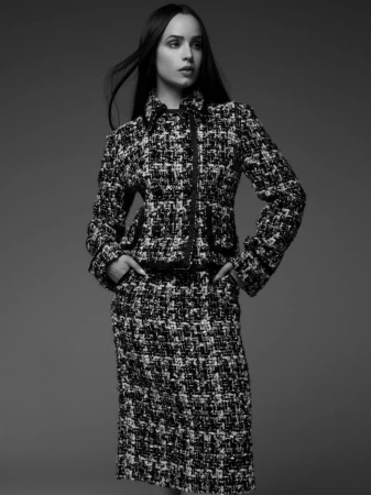 Black and white studio portrait of a woman with long dark hair wearing a textured skirt suit with a high collar and zipped jacket.