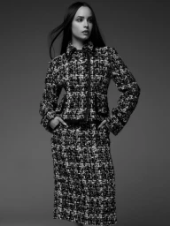 Sofia Carson wearing a textured tweed jacket and skirt suit in a black and white studio portrait.