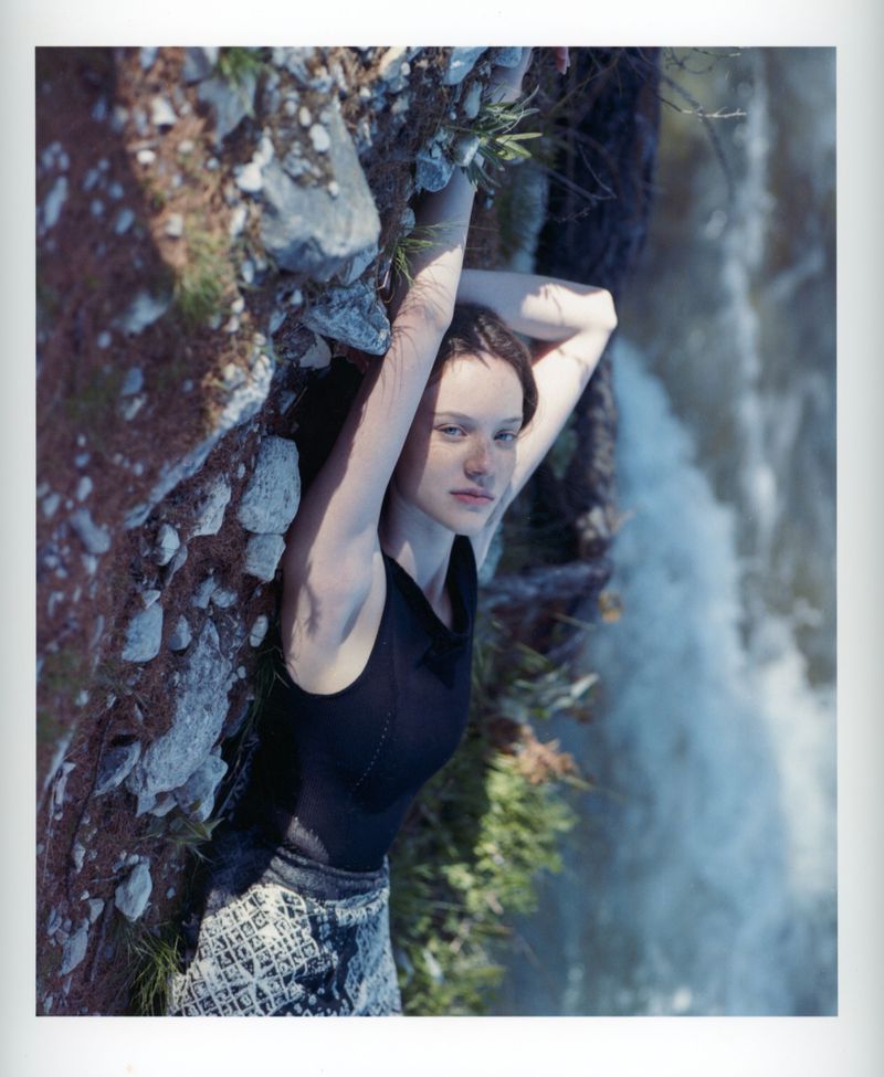 Woman in a black sleeveless top lying along a rocky bank beside rushing water for Lula Japan.