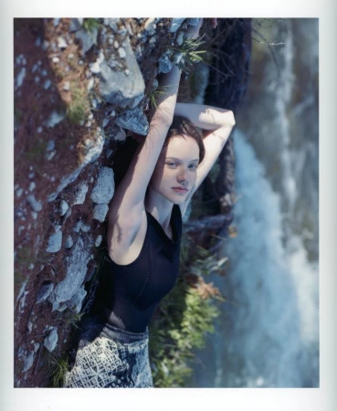 Woman in a black sleeveless top lying along a rocky bank beside rushing water for Lula Japan.