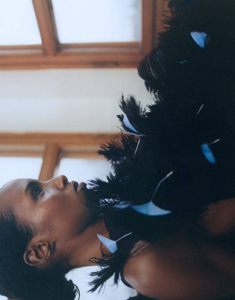 Portrait of a stylish woman with an elaborate feather boa looking up against a light background with a window frame.