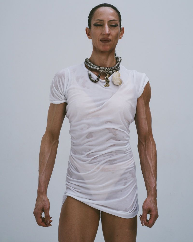 Woman in a white t-shirt dress and necklace poses in a studio. Close up shot of a dark-haired woman in a short dress.