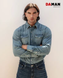 Model Chand Smith wearing a blue denim shirt with arms crossed against a plain light background for DA MAN Magazine